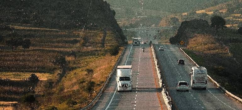 Vehicles driving on a rural highway through dry, wooded hills at dusk