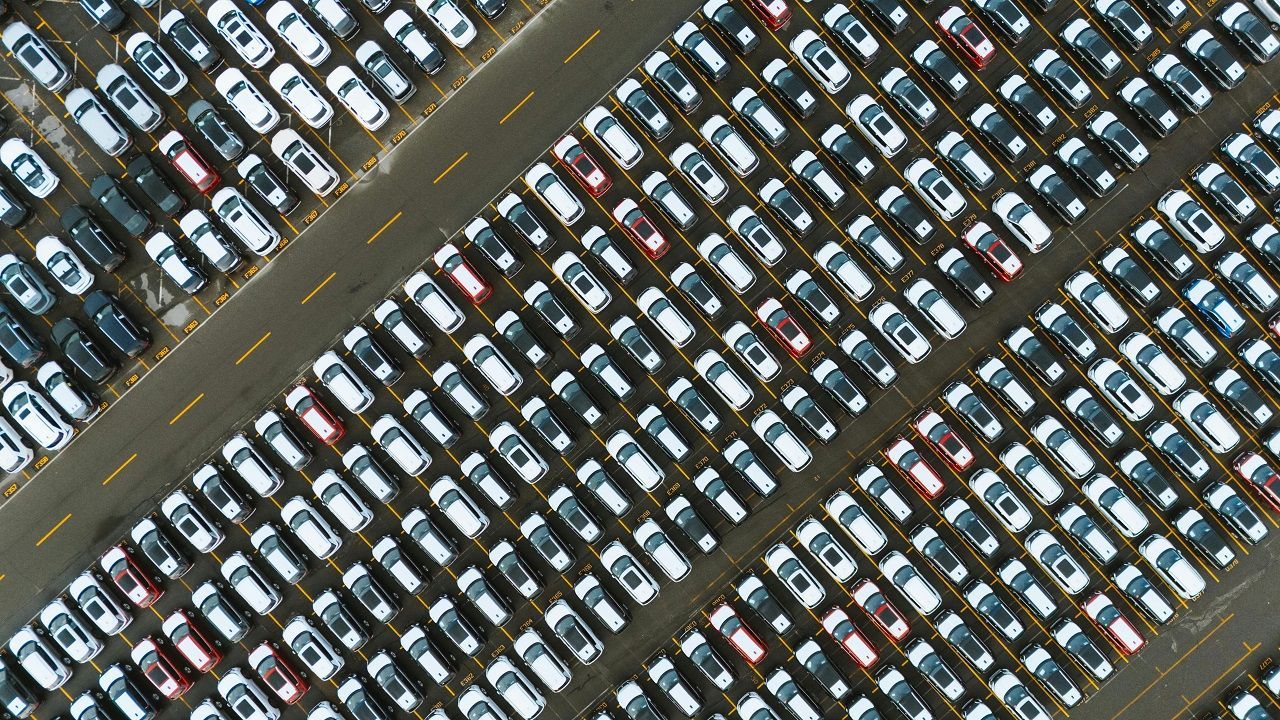 Aerial view of a large parking lot filled with tightly packed white and dark-colored cars.