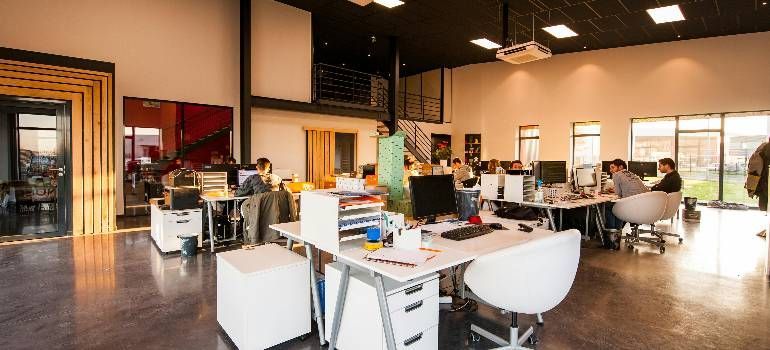Open-plan office with desks, computers, chairs, and people working in a bright modern workspace