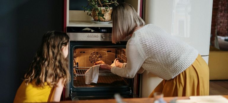 Woman and child baking together at a kitchen oven, using a tray in the warm-lit interior
