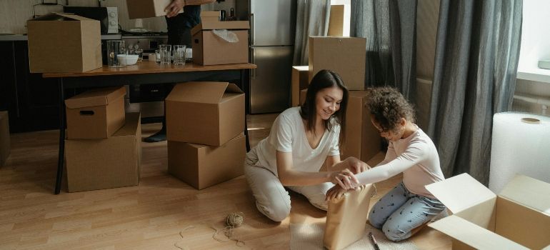 Two people unpacking boxes in a living room with cardboard boxes and a laptop on a desk