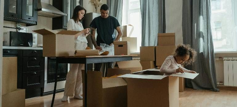People unpacking boxes in a bright apartment while a child sits inside one box