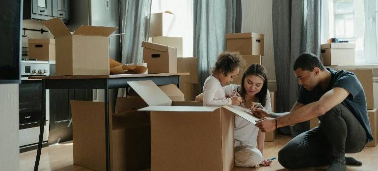 Family unpacking moving boxes in a bright living room with a laptop nearby