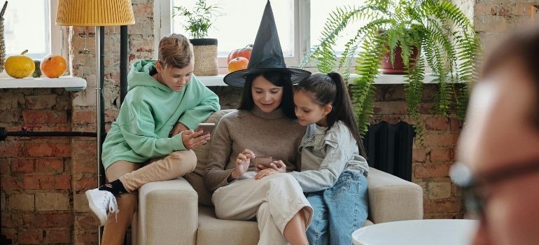 Three people sit on a sofa reading together in a cozy living room with plants and a brick wall.