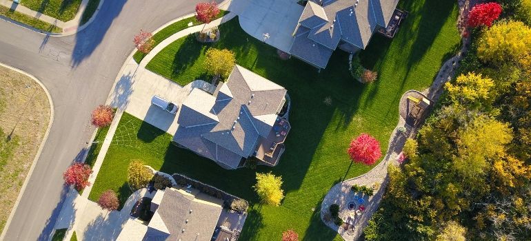 Aerial view of suburban homes with green lawns, curving streets, and trees in fall colors