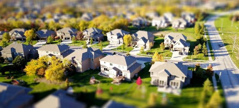Aerial view of a suburban neighborhood with houses, trees, and a road on the right.