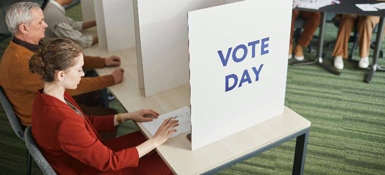 Voter filling out ballot at a polling station beside a sign reading “VOTE DAY”