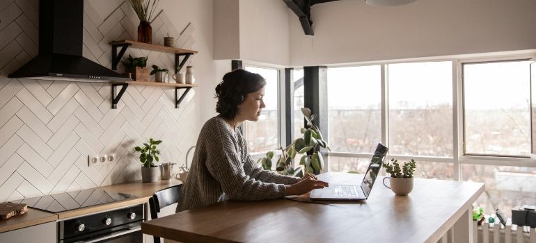 Person working on a laptop at a wooden kitchen island in a bright, modern kitchen