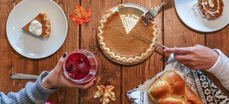 Top-down view of a Thanksgiving dessert table with pie, wine, and bread on a wooden table