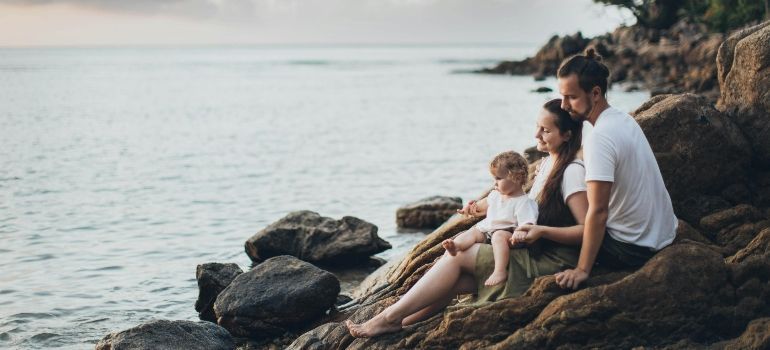 Family sitting on rocks by the calm sea at sunset