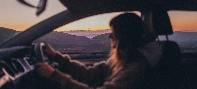 Person driving a car at sunset, looking out toward a desert landscape