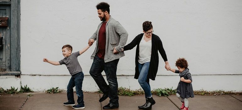 Family holding hands and walking together outdoors beside a white wall