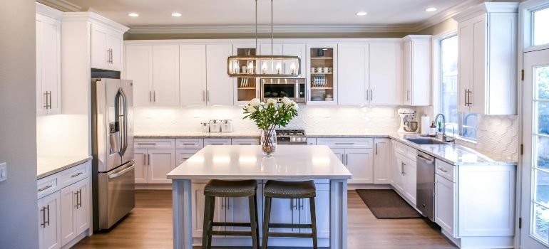 Bright white modern kitchen with a large island, bar stools, and stainless steel appliances.