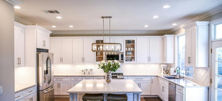 Bright modern white kitchen with island, pendant lights, stainless appliances, and large windows