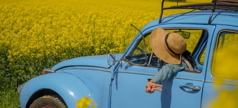 Yellow convertible in a flower field with a person leaning out the window, wearing a straw hat.
