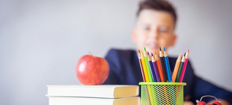 Apple on stacked books beside a pencil cup, with a blurred person in the background