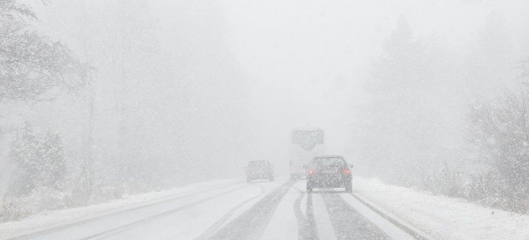 Cars driving on a snow-covered road in heavy fog or blizzard conditions