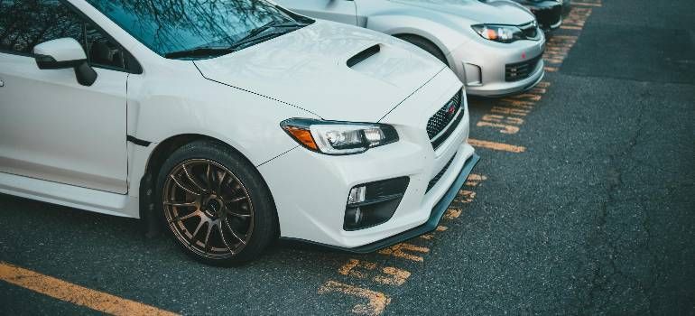 Two white parked sports cars in a parking lot, front car with black rims and yellow curb markings