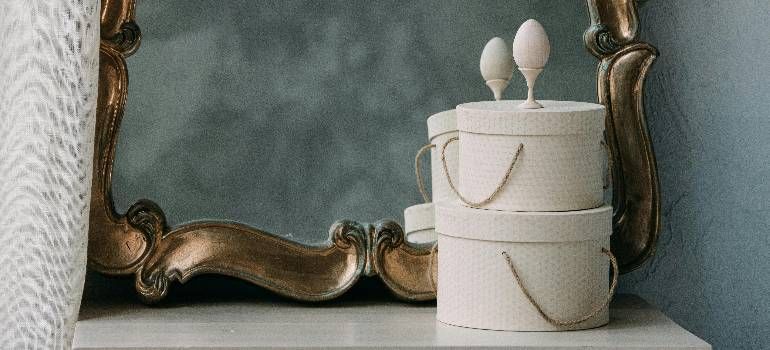 Stacked white gift boxes with bows beside an ornate mirror on a white table