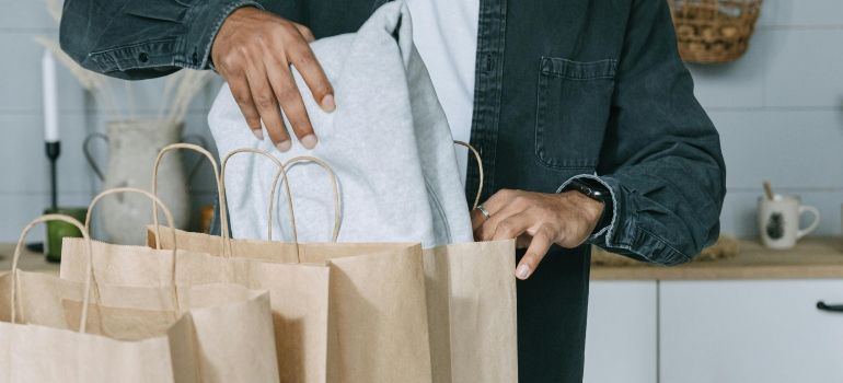 Person placing white packages into brown paper shopping bags on a kitchen counter