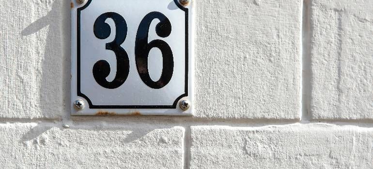White house number plaque reading 36 on a light stone wall