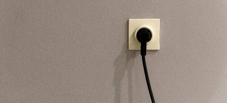 Black cable plugged into a white wall outlet on a gray wall.