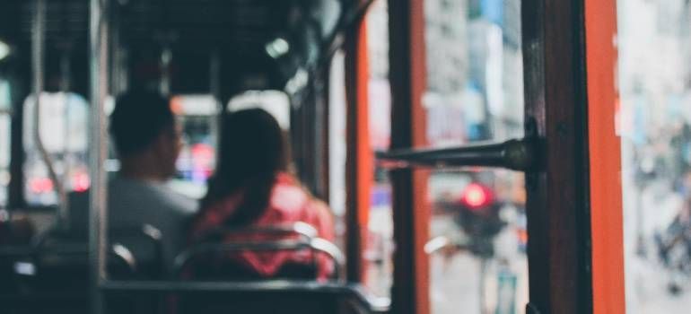 Blurred view from a bus: two seated passengers and orange poles by the window.