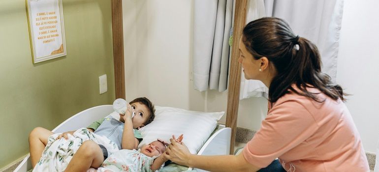 Caregiver talks to a child lying in a hospital bed with a teddy bear nearby