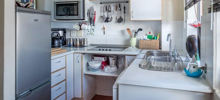 Bright white kitchen with a refrigerator, sink, dish rack, and countertop appliances