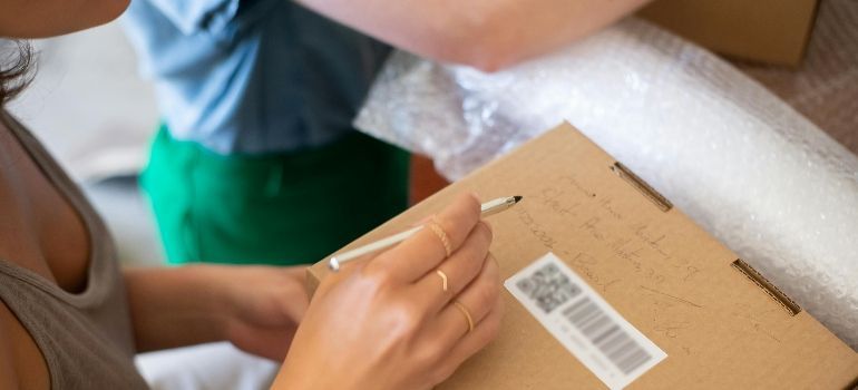 Person sealing a cardboard package with tape beside bubble wrap and a barcode label