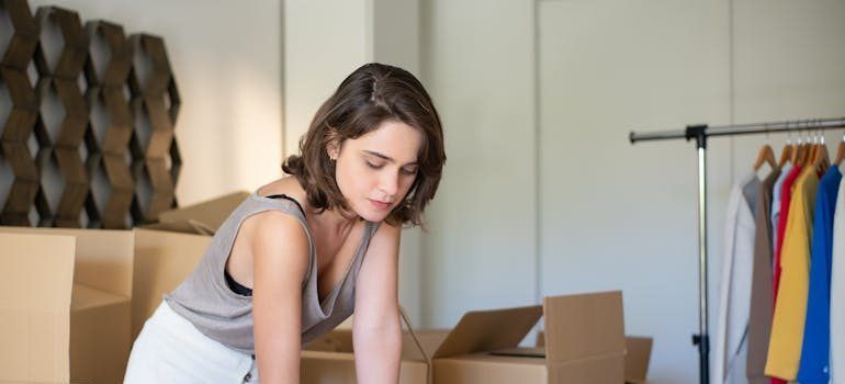 Person packing boxes in a room beside a clothing rack and patterned wall décor