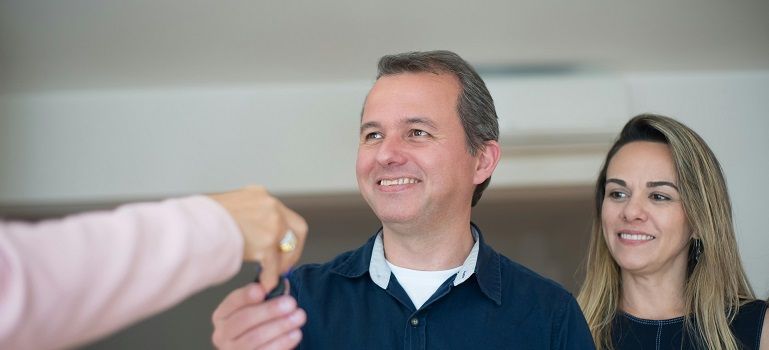 Two smiling people looking at an outstretched hand holding a small key
