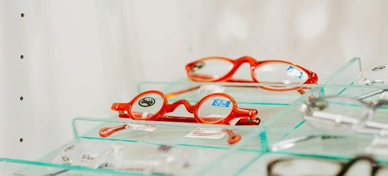 Several pairs of orange-framed eyeglasses displayed on a glass shelf