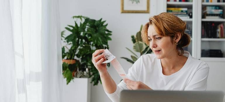 Woman in a white shirt examining a small vial at a desk in a bright home office