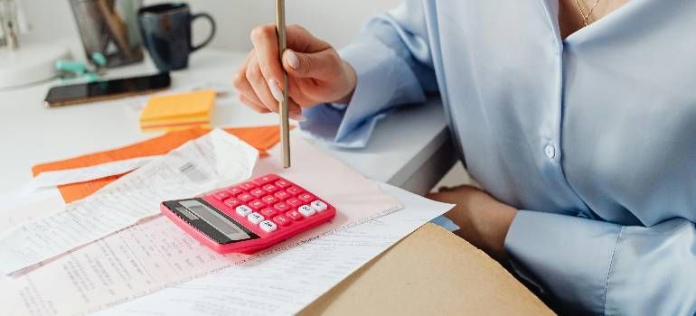 Person writing with a pencil beside a red calculator on papers at a desk