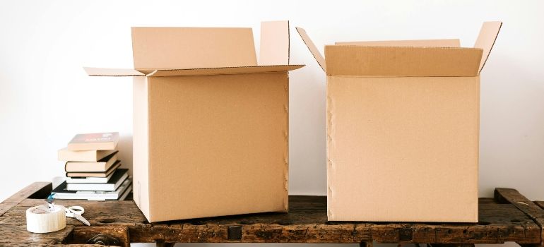 Two open cardboard moving boxes on a table, with stacked books and packing tape nearby.