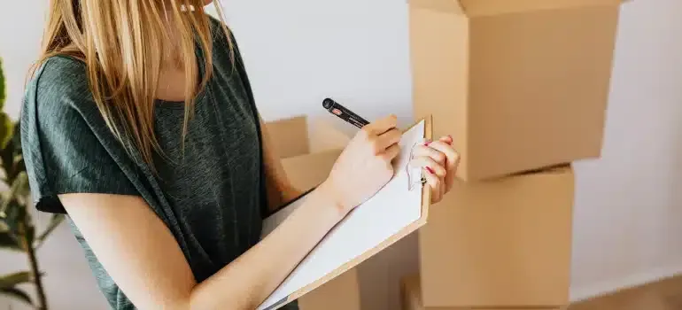 Person writing on a clipboard beside stacked cardboard moving boxes