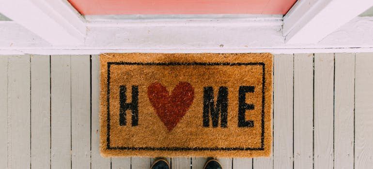 Doormat with “HOME” and a heart symbol on a white porch floor, viewed from above