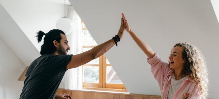 Two people high-five in a bright room by a window