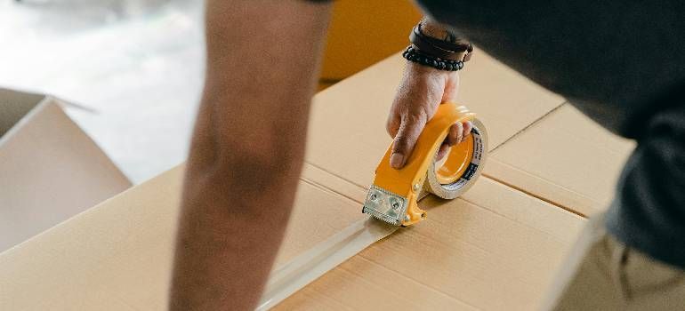Person using a tape dispenser to seal a cardboard box during packing.