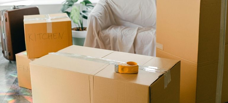 Person packing cardboard boxes in a bright room, with a tape dispenser on the box in front