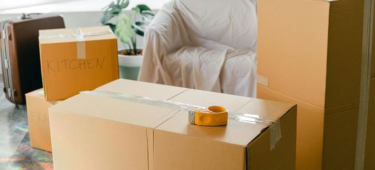 Packed cardboard boxes in a room, with a small orange tape dispenser on one box.