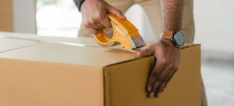 Hands sealing a cardboard box with orange packing tape