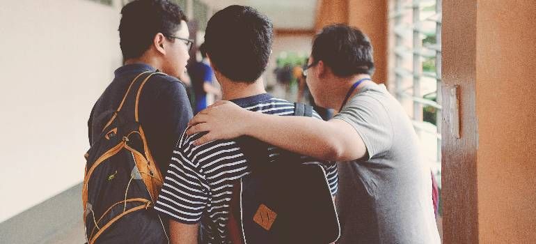 Three friends with backpacks walking together outdoors, one with an arm around the other.