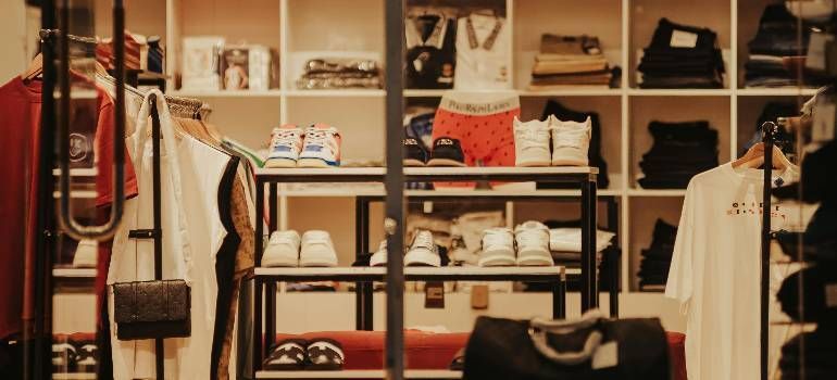 Clothing store display with shelves of folded clothes, hanging garments, and accessories in warm lighting
