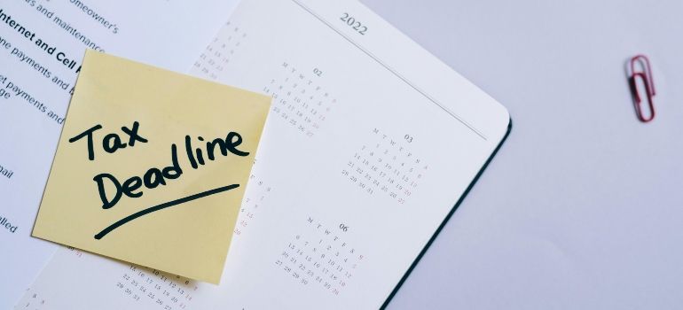 Sticky note reading “Tax Deadline” on a calendar page with paperclip on a light desk.