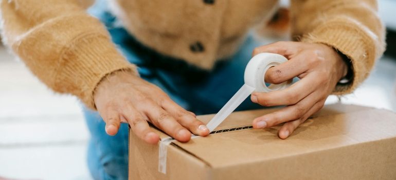 Hands using a white tape dispenser to seal a cardboard box