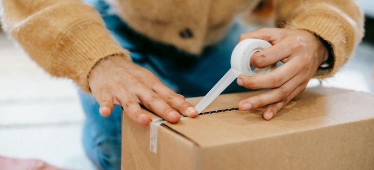 Hands sealing a cardboard box with white packing tape during packing.