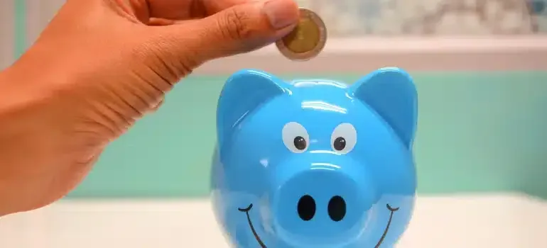 Hand holding a coin above a blue piggy bank with a smiling face