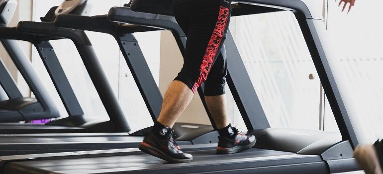Person running on a treadmill in a gym, wearing black shoes and red-striped leggings